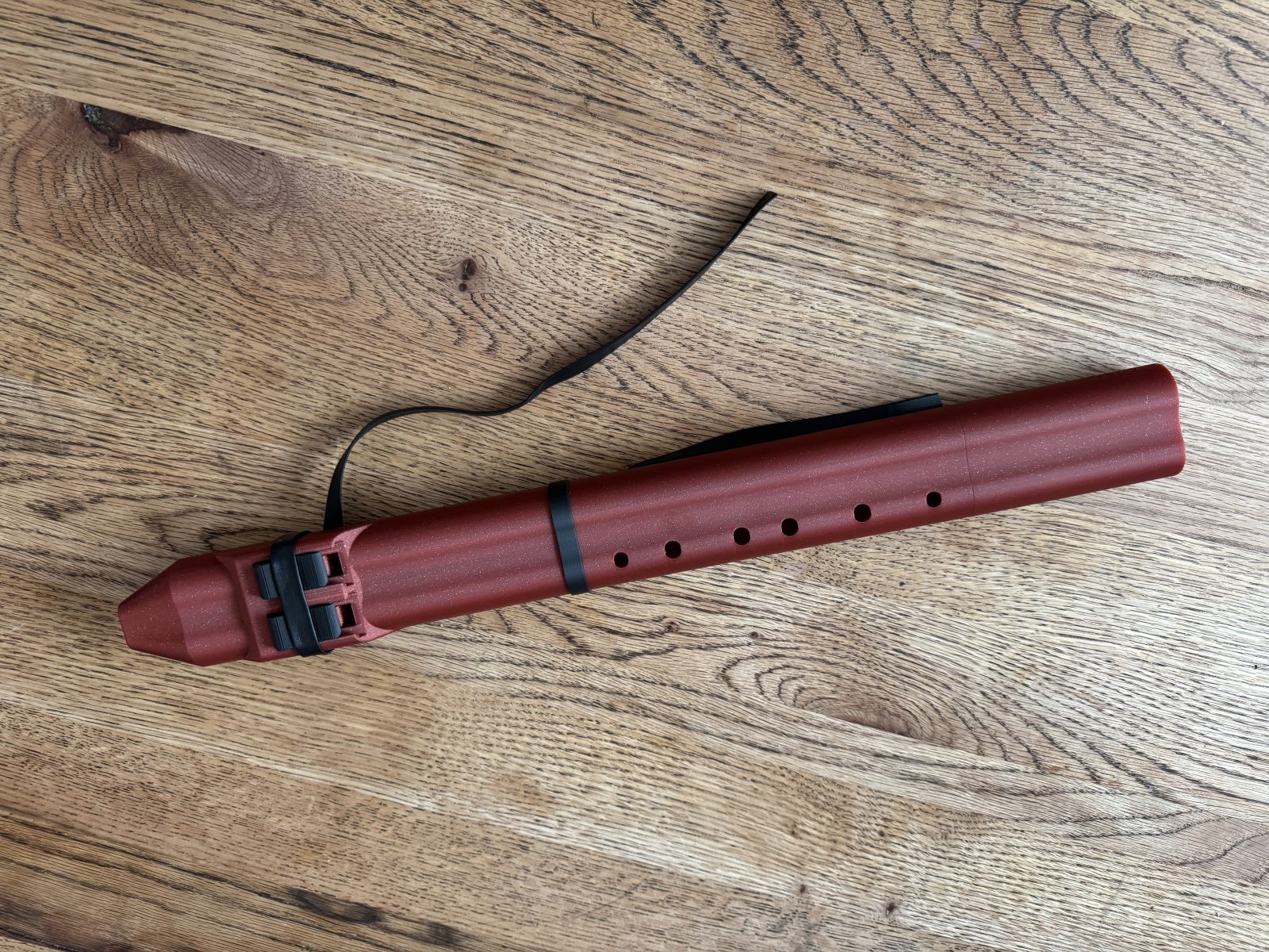 Crimson double drone flute in A seen from above on an oak floor, with two blocks at the head and six finger holes along one side
