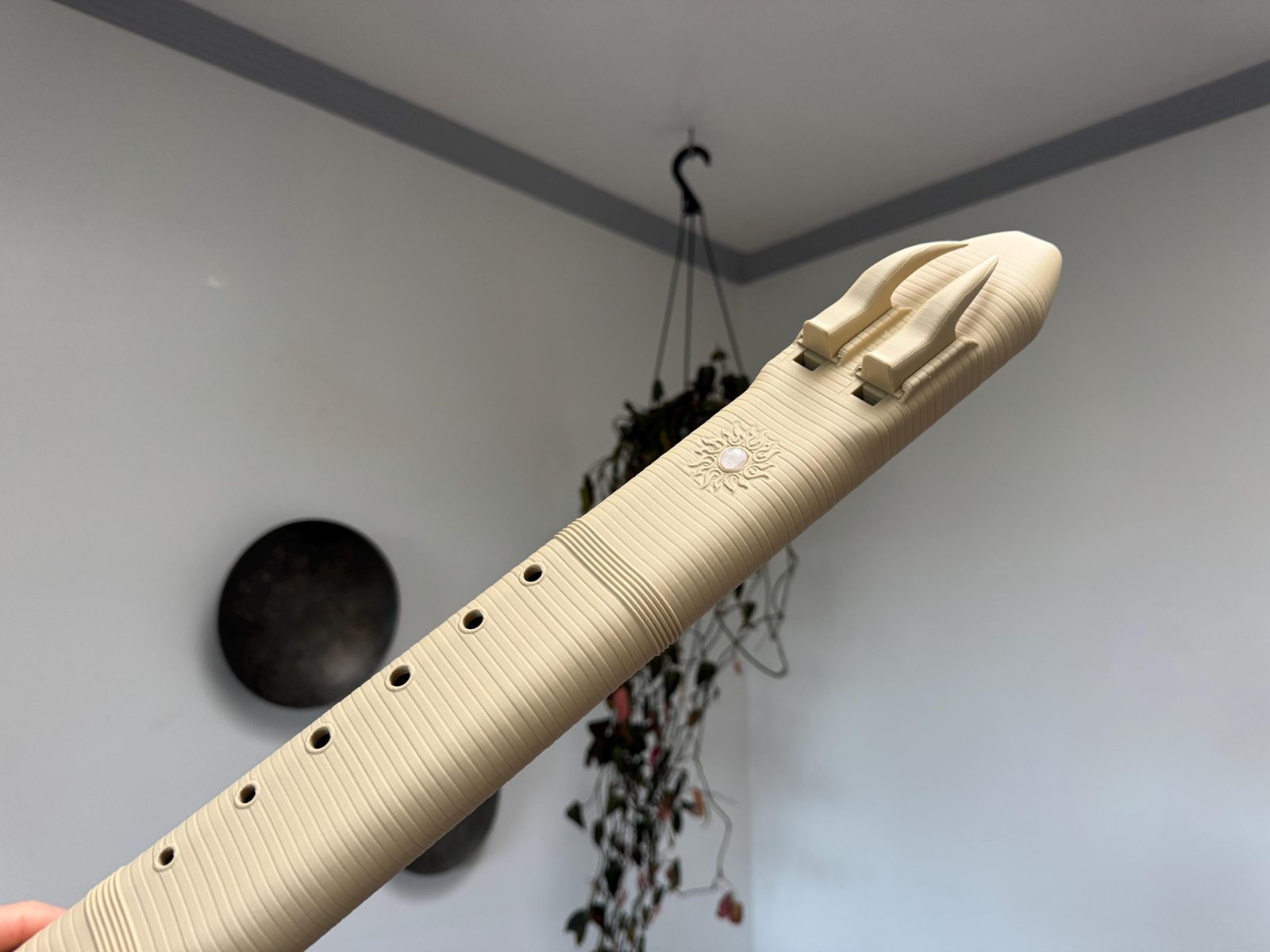 Cream Desert Rose drone flute held at an angle, with its ridged body, two horn-shaped blocks and a sun medallion set with rose quartz
