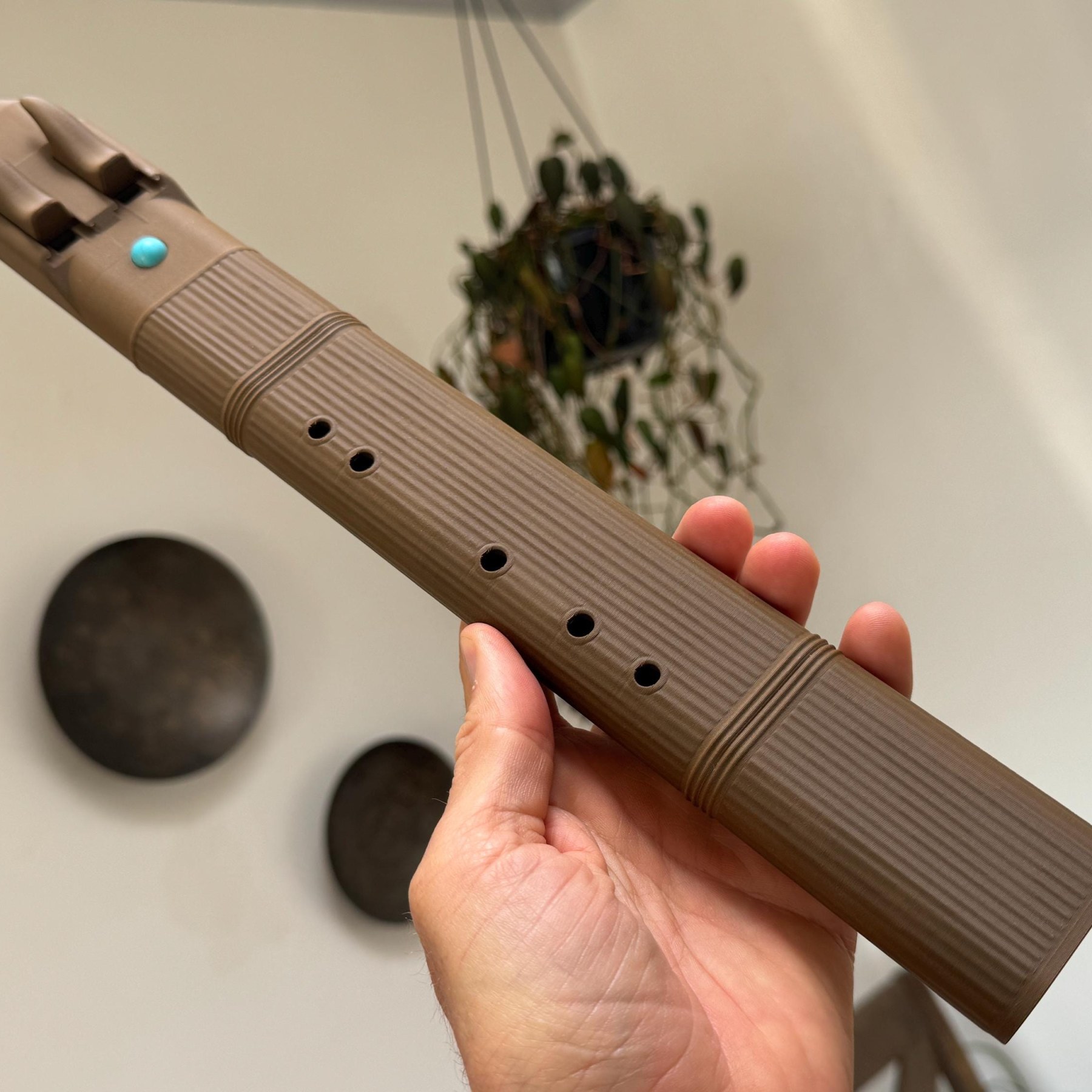 Brown wood PLA B4 drone flute held in one hand, showing finger holes, ridged body, horn-shaped blocks, and turquoise accent