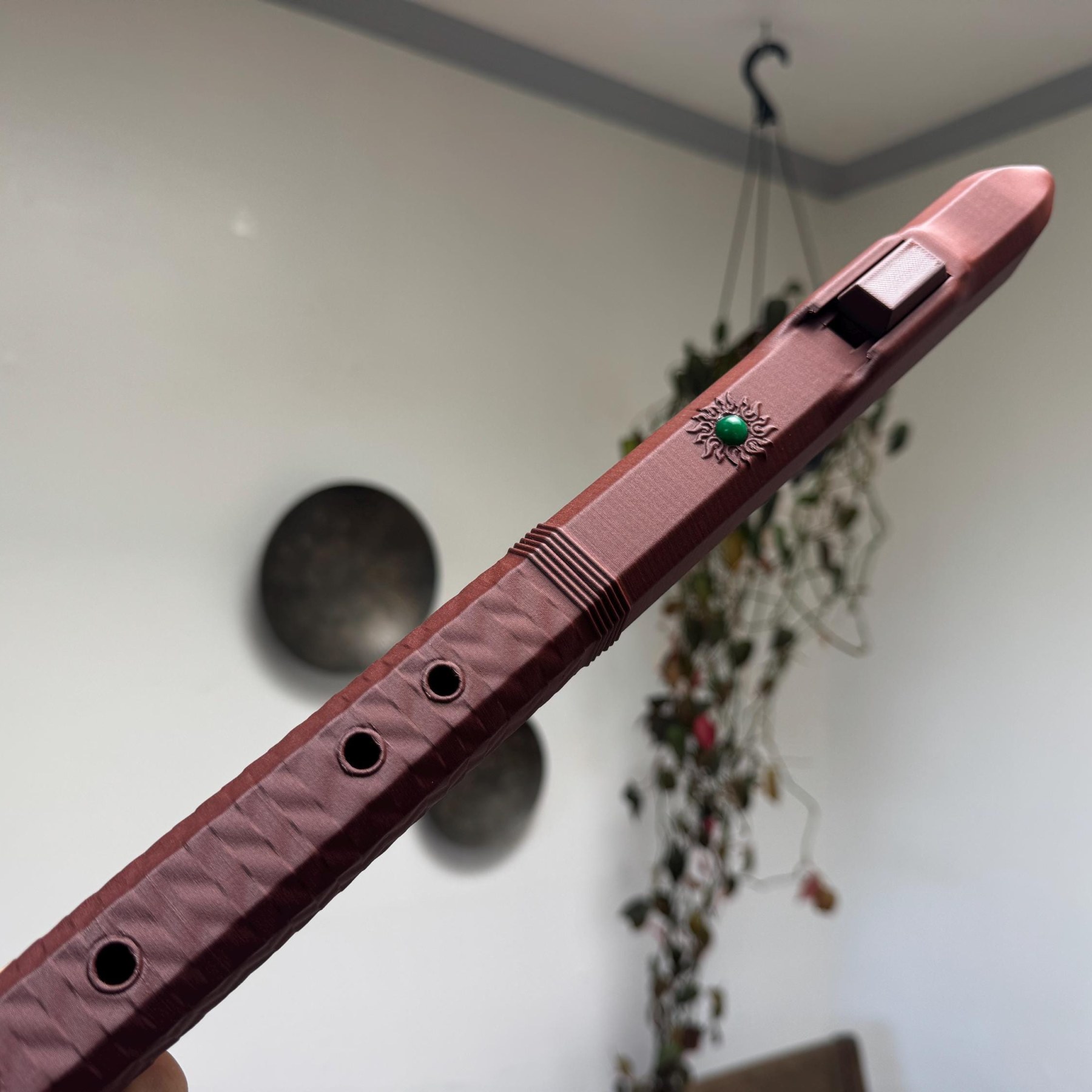 Deep red F sharp 4 Native American style flute held at an angle, showing finger holes, ribbed band, block, and green stone emblem