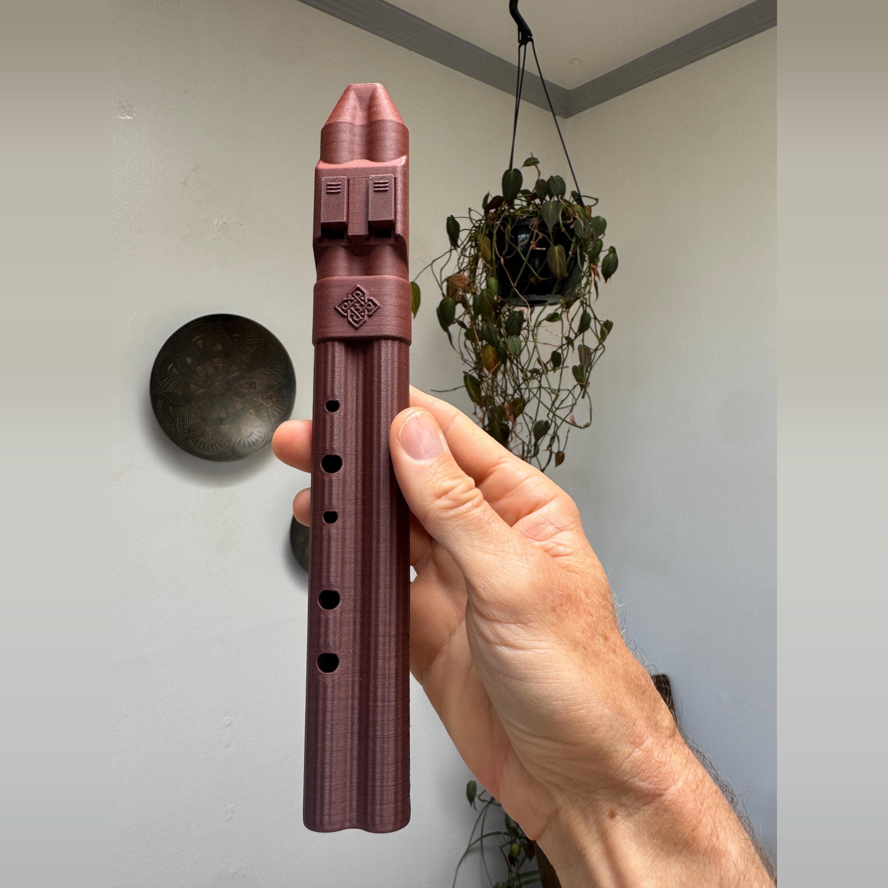 F sharp 5 pocket drone flute held upright in one hand, deep burgundy 3D-printed body with two sound blocks and a knotwork band