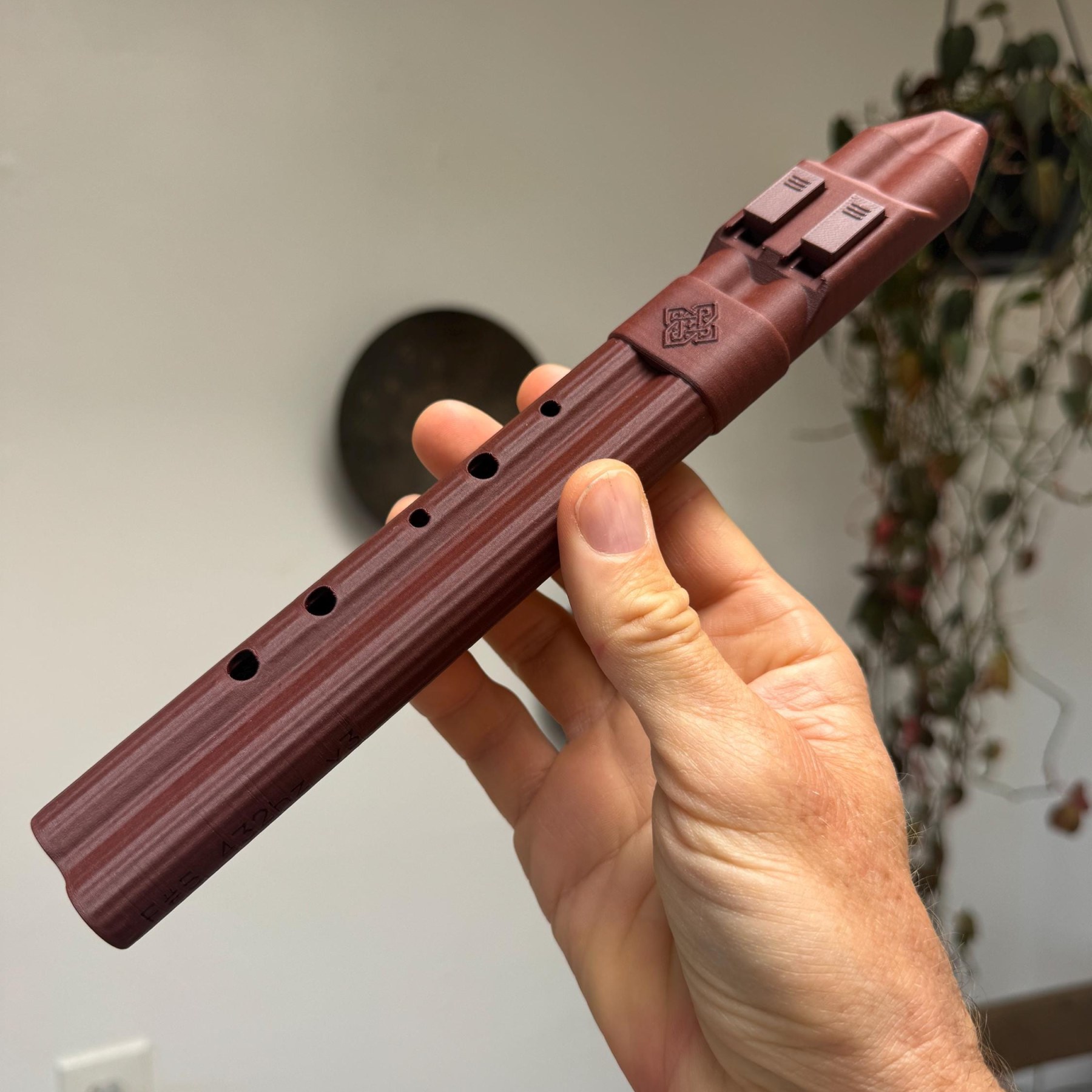 Pocket drone flute held at an angle, showing its finger holes and the knotwork band below the mouthpiece