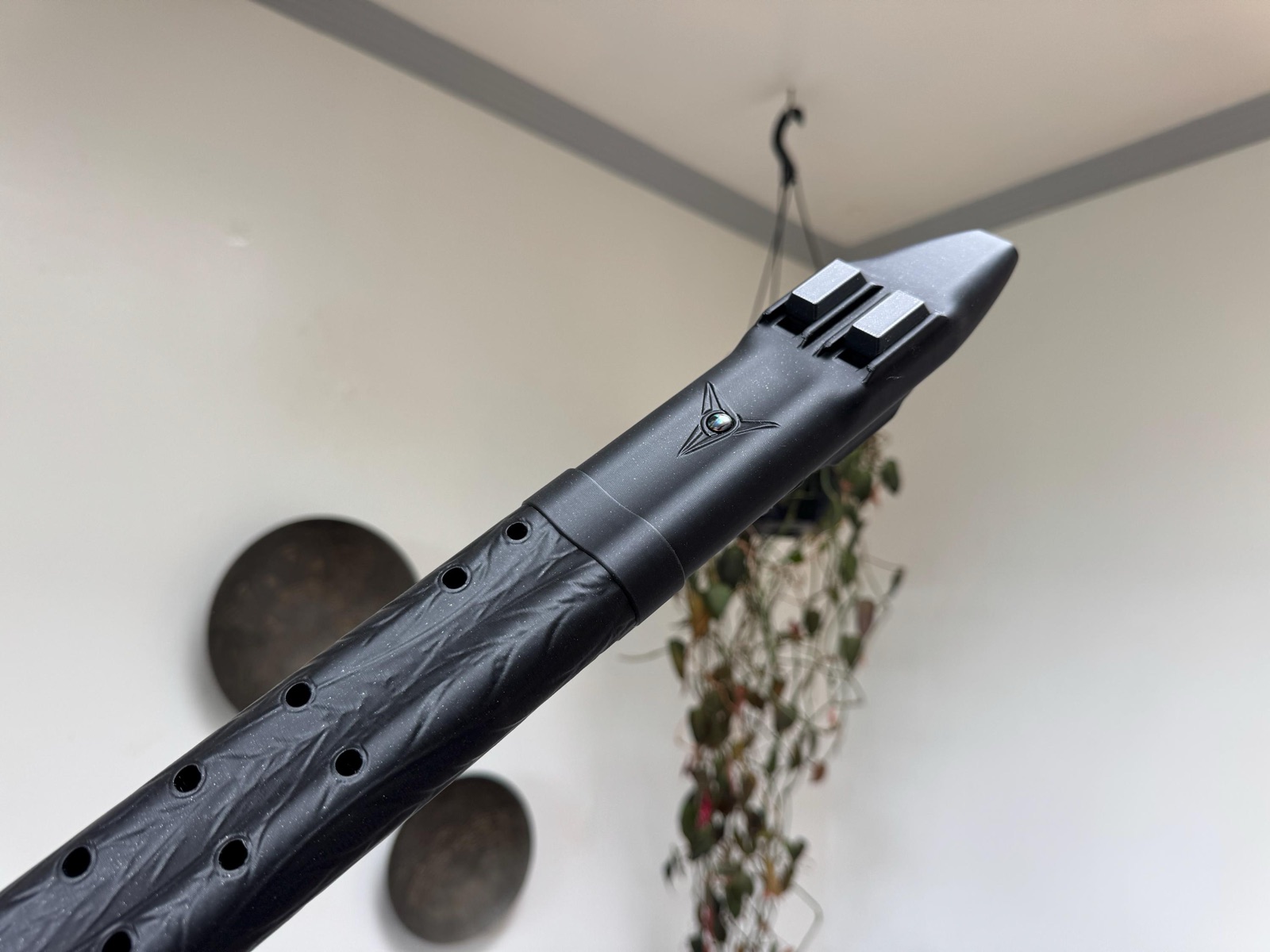 Raven triple drone flute from an angle, showing the feather-textured playing section with finger holes below the smooth upper body