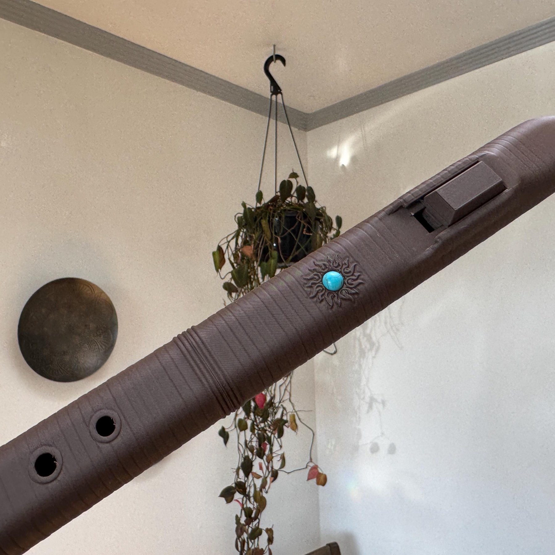 Dark brown wood PLA triangle flute held at an angle, showing the block, turquoise sun emblem, and finger holes