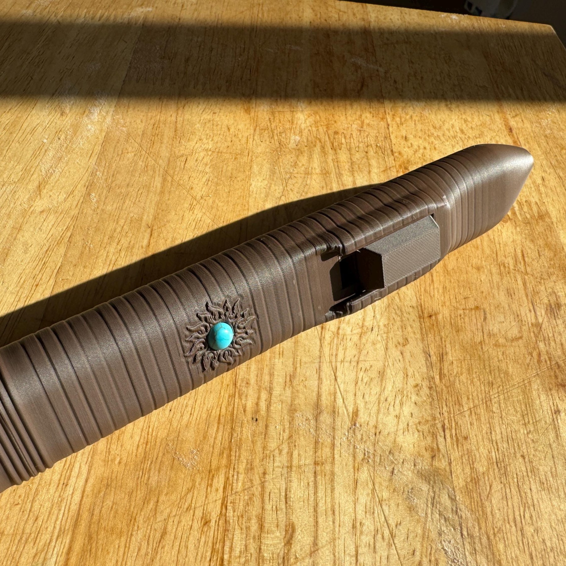 Triangle flute mouthpiece and turquoise emblem on a wooden table in sunlight