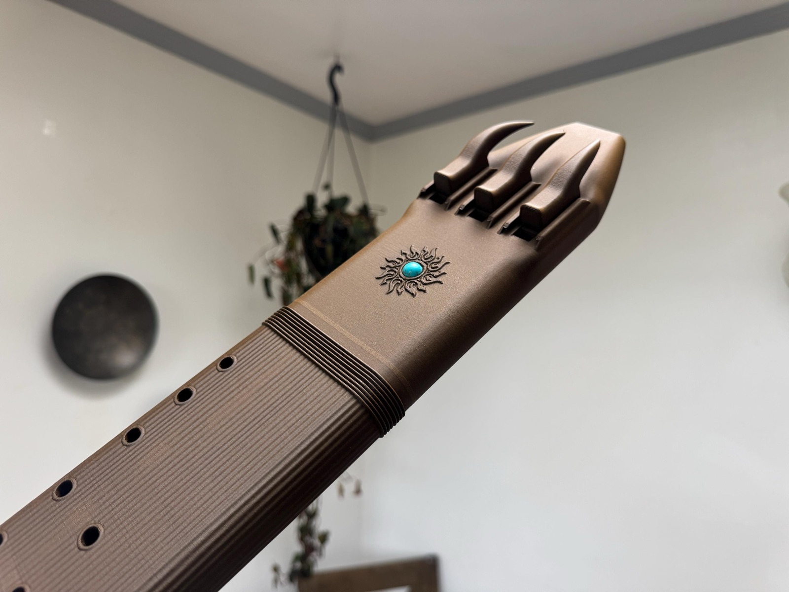Brown wood PLA F sharp 4 triple drone flute from an angle, showing three curved blocks and a sun motif with a turquoise-colored inlay