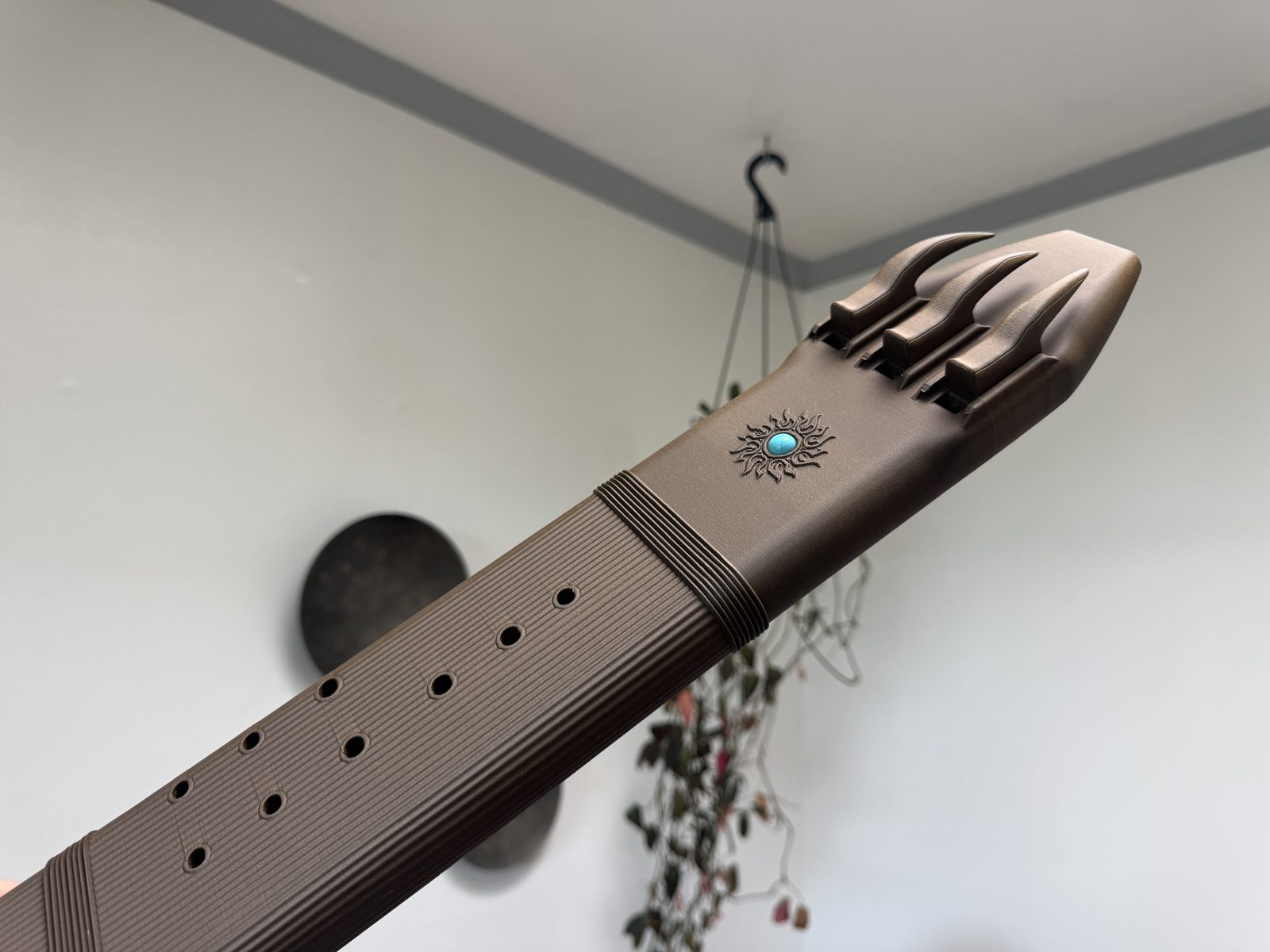 Brown wood PLA F sharp 4 triple drone flute held at an angle, showing its three curved blocks, sun motif with a turquoise-colored inlay, and finger holes